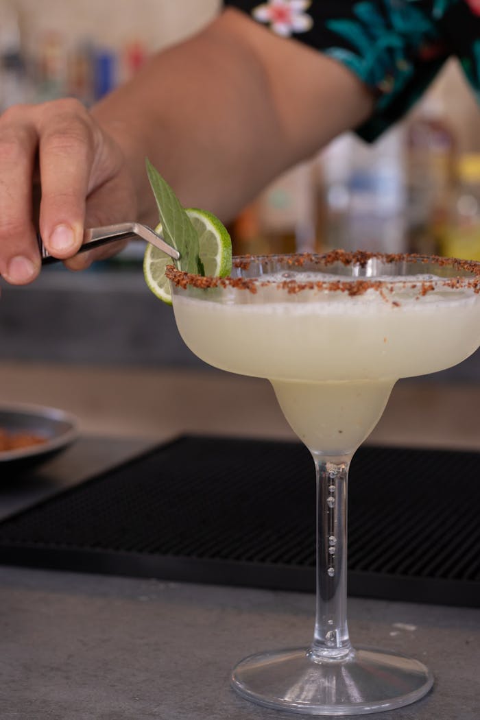 Close-up of a margarita being garnished with lime and herbs, perfect summer cocktail.