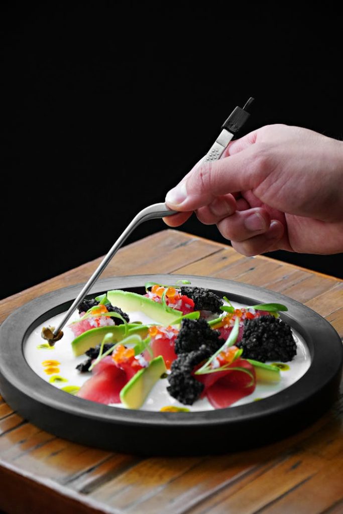 Close-up of a gourmet dish with vibrant garnish being carefully arranged by a chef's hand.