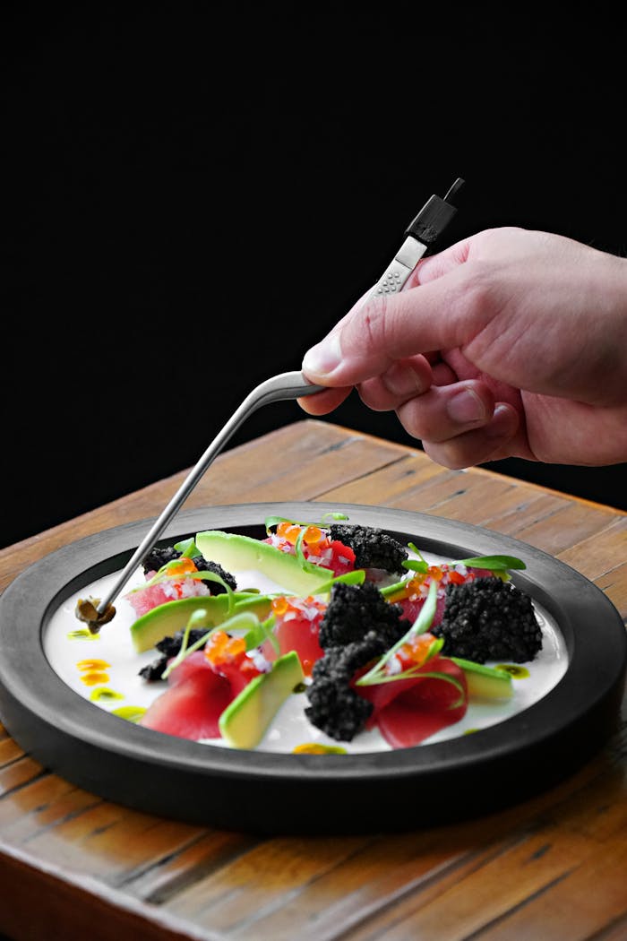 Close-up of a gourmet dish with vibrant garnish being carefully arranged by a chef's hand.