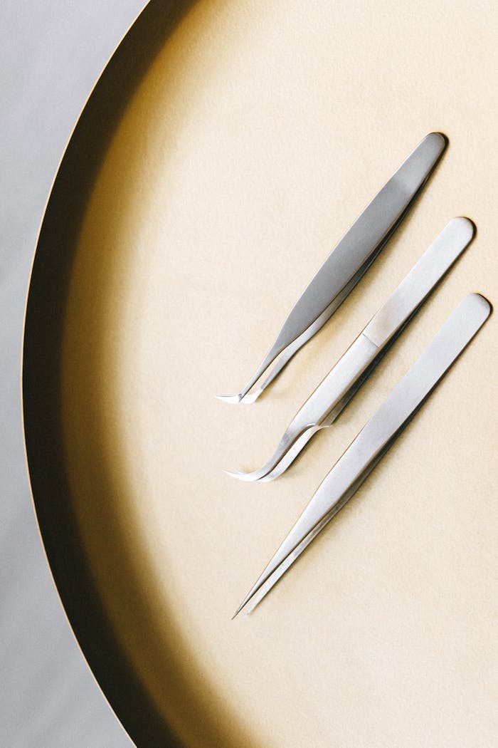 High angle view of three stainless steel tweezers on a flat circular surface.