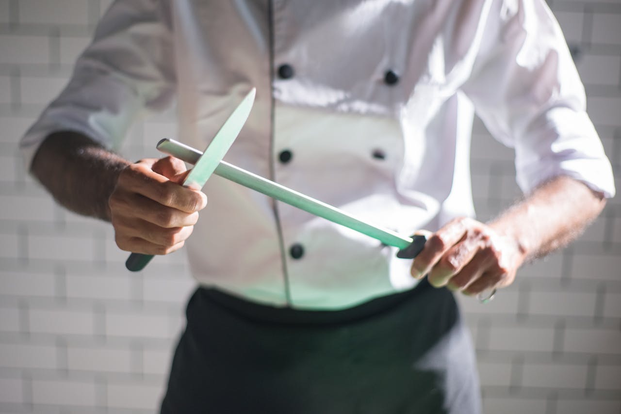 Close-up of a chef sharpening a knife with a honing rod in a modern kitchen setting.