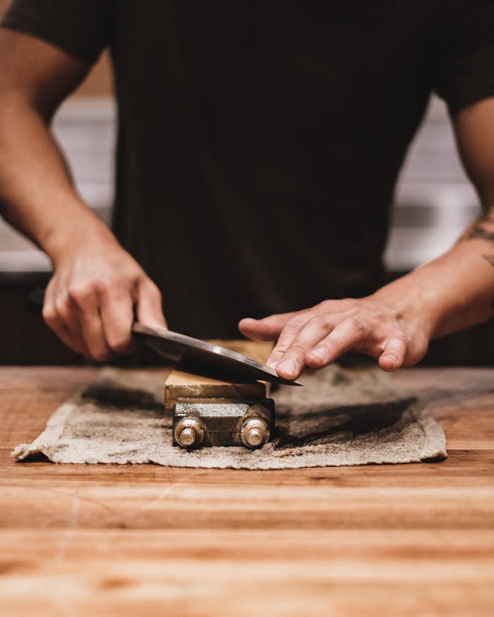 A person sharpening a knife on a whetstone in an indoor setting. Focus on hands and technique.